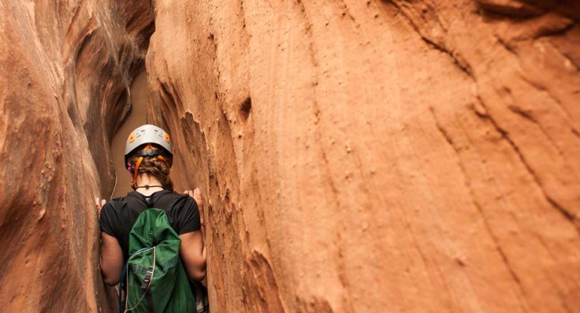 a person wearing a helmet maneuvers through a slot canyon